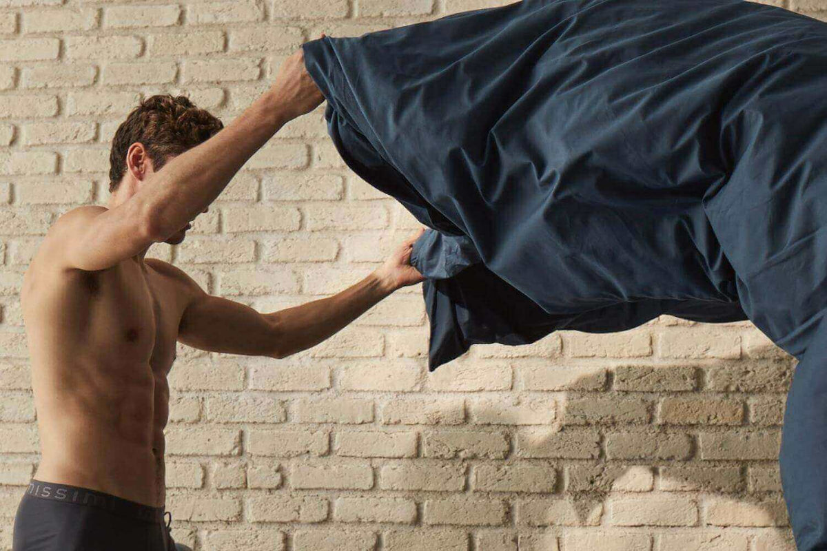 Man shaking out a navy duvet cover in front of a whitewashed brick wall