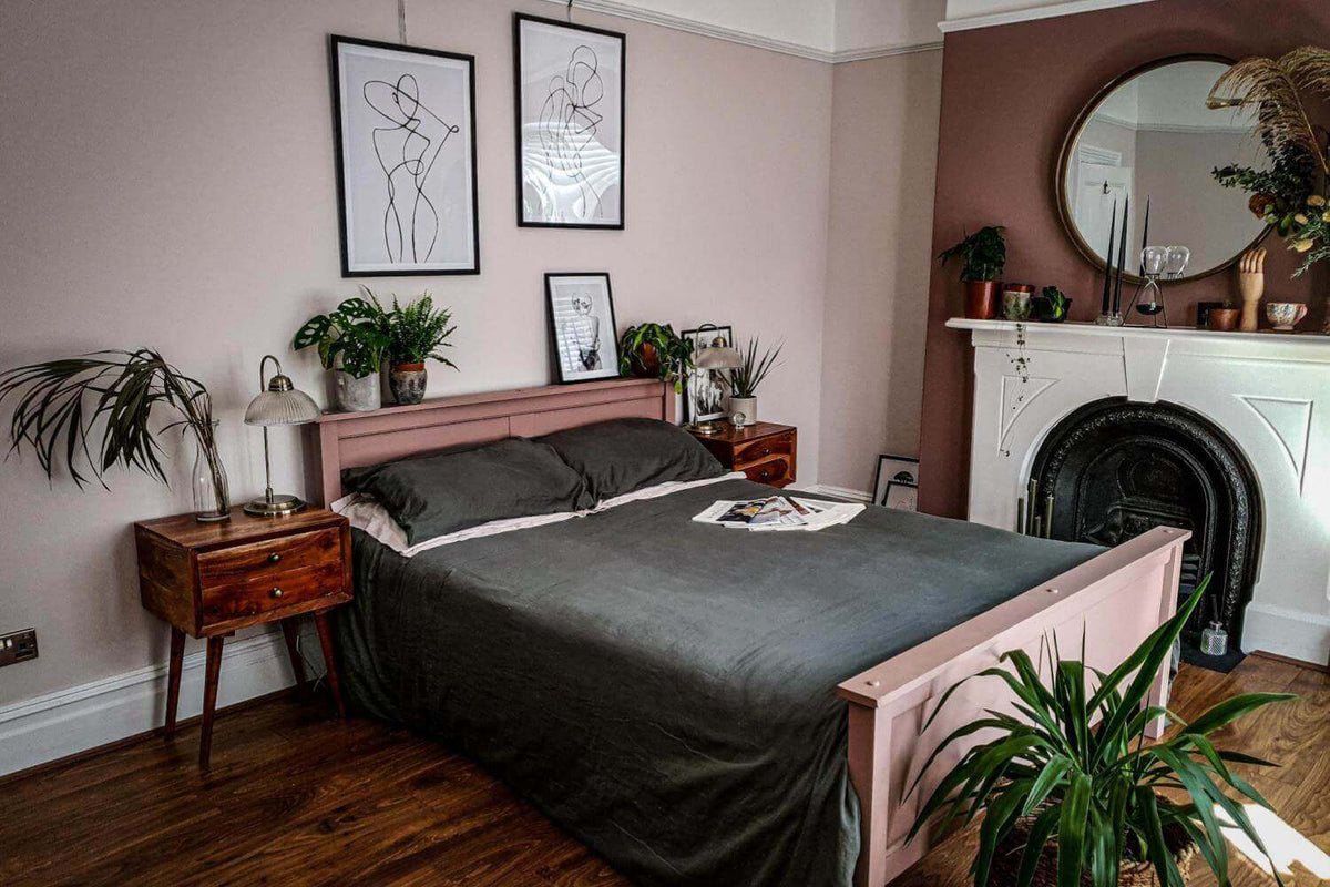 Bedroom with a pink bed frame, dark grey bedding, framed line art prints and a cast iron fireplace