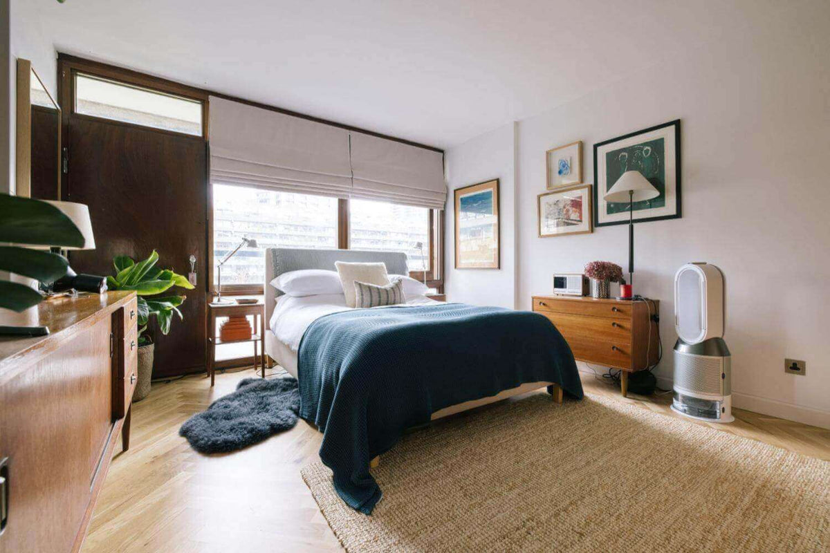 Bright bedroom with a navy throw on the bed, framed prints, a jute rug and a wooden sideboard