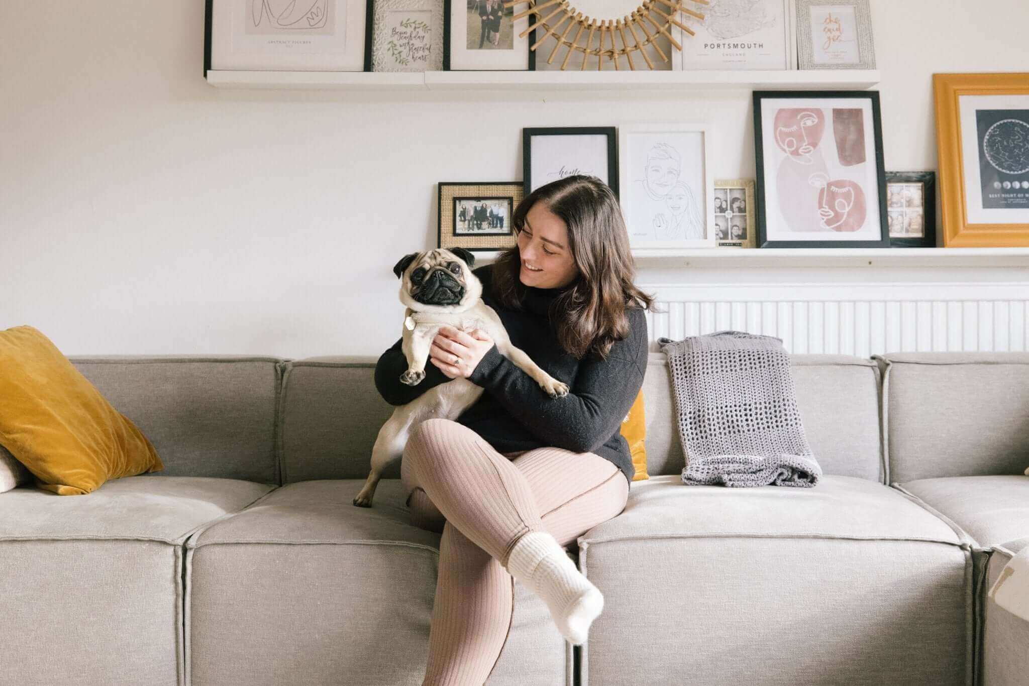 Woman holding a pug dog on a cozy sofa in a stylish, pet-friendly living room.