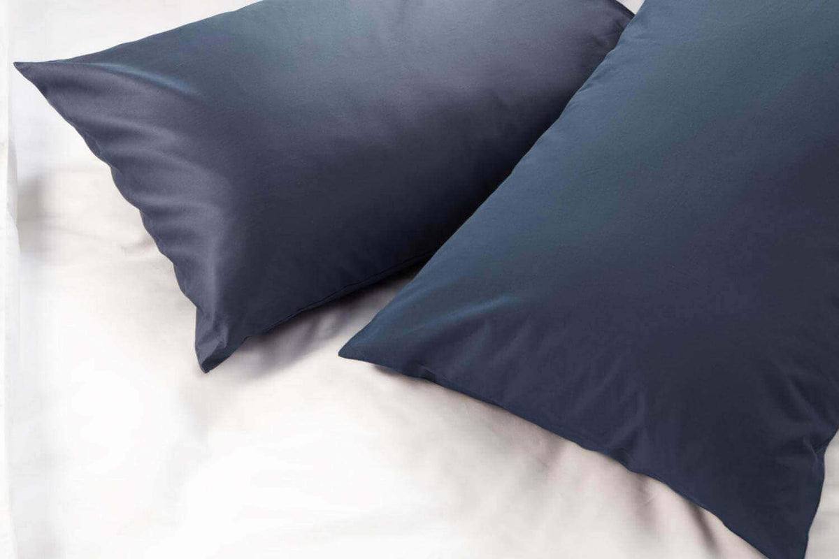 Close up of two navy pillowcases resting on a crisp white sheet