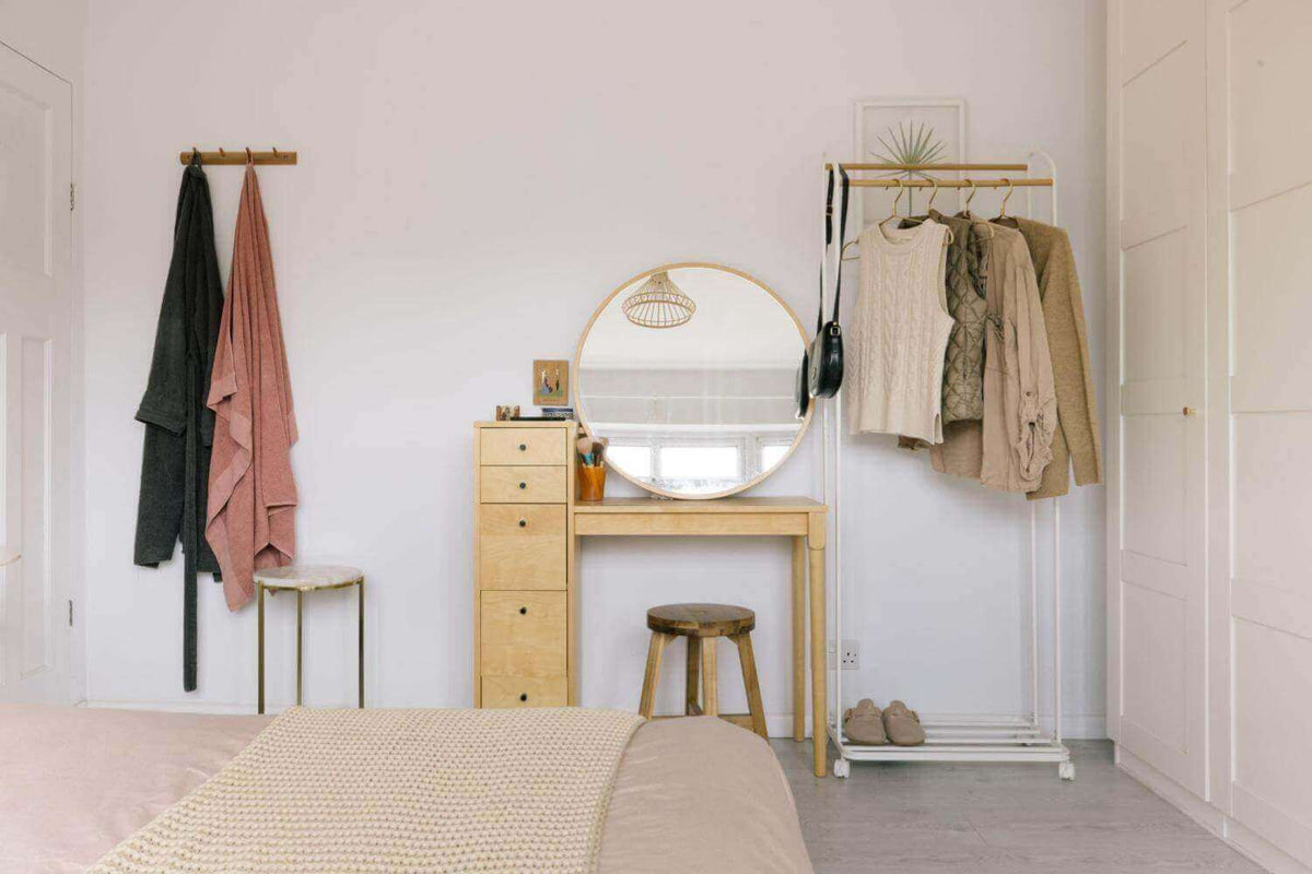 Bright bedroom corner with a dressing table, round mirror, wall hooks and a clothes rail