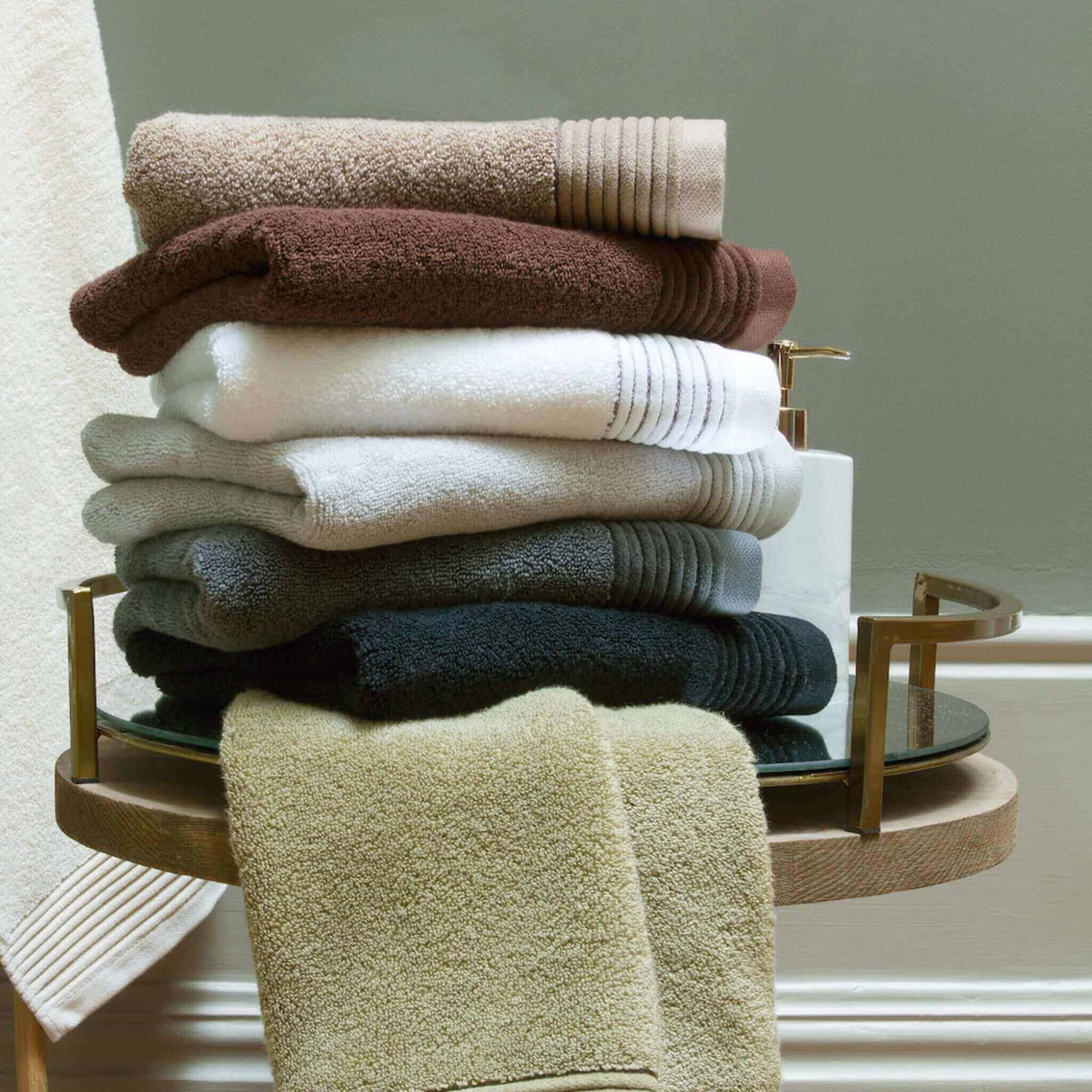 Stack of folded cotton towels in brown, white, grey and sage on a brass stand