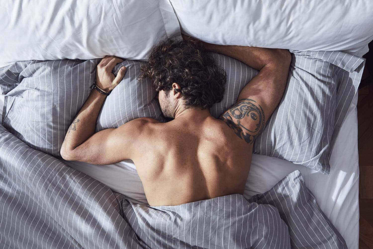 Man sleeping restlessly in bed surrounded by pillows and covers, illustrating challenges of sharing a bed.