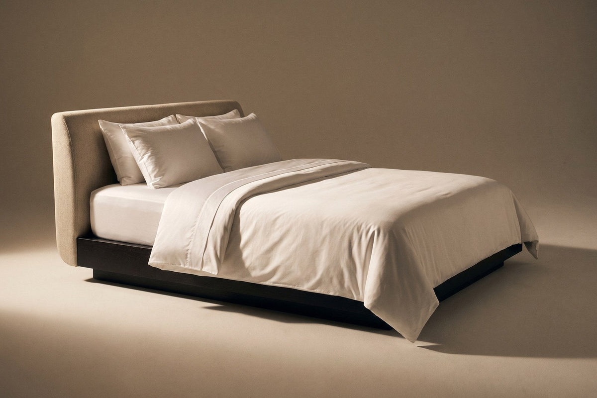 Bed with white sateen bedding on a dark plinth base against a warm beige backdrop
